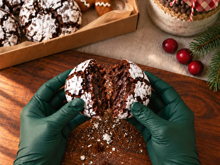 Gloved hands breaking a chocolate crinkle cookie